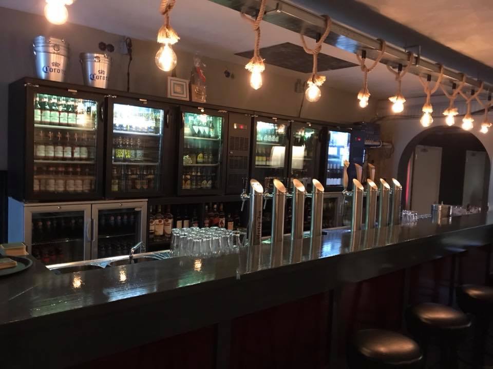 De bar van Logan's Pub met tapkranen, koelkasten en Edison-lampen