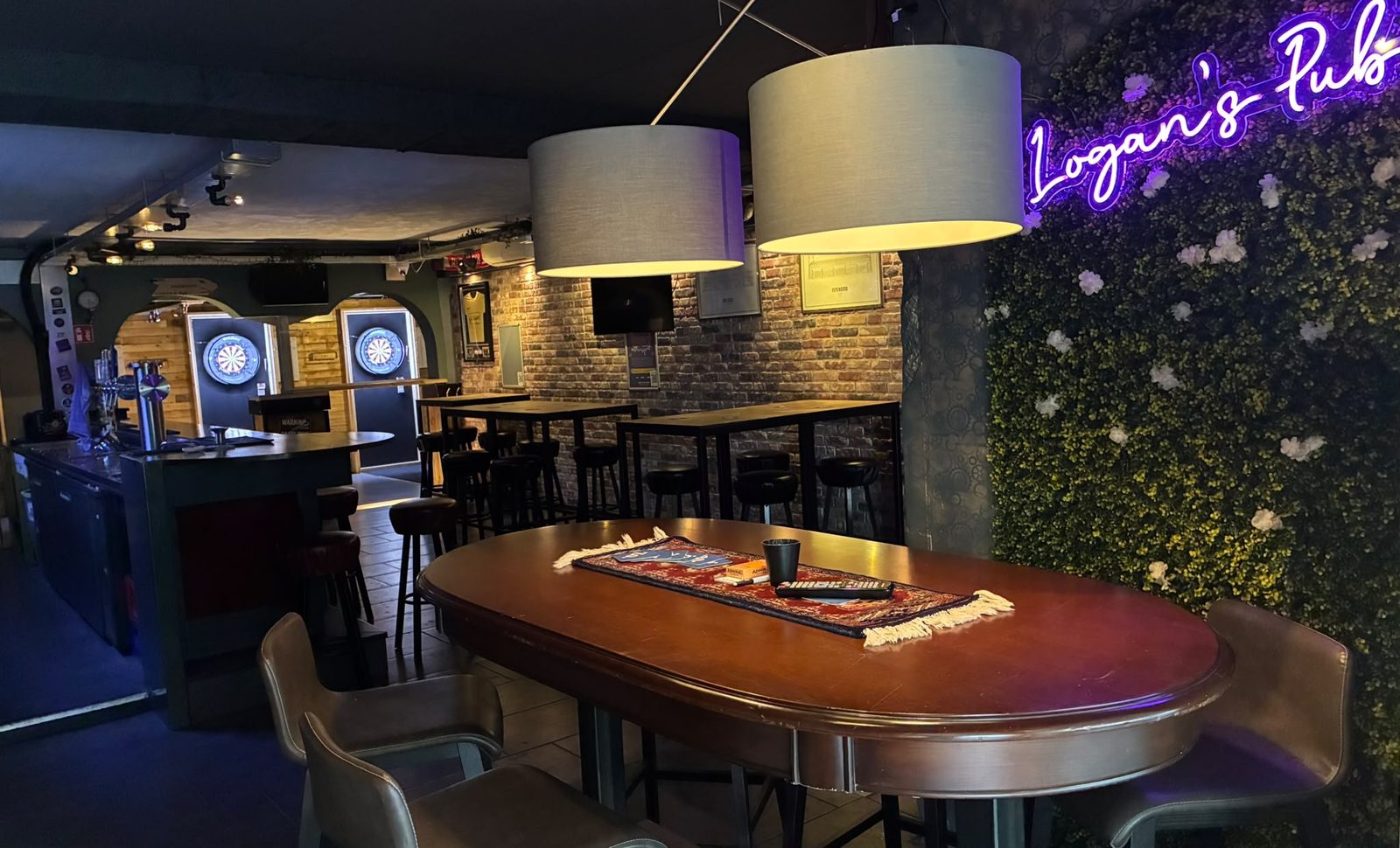Binnen bij Logan's Pub: lange tafel, bartafels en de darthoek op de achtergrond